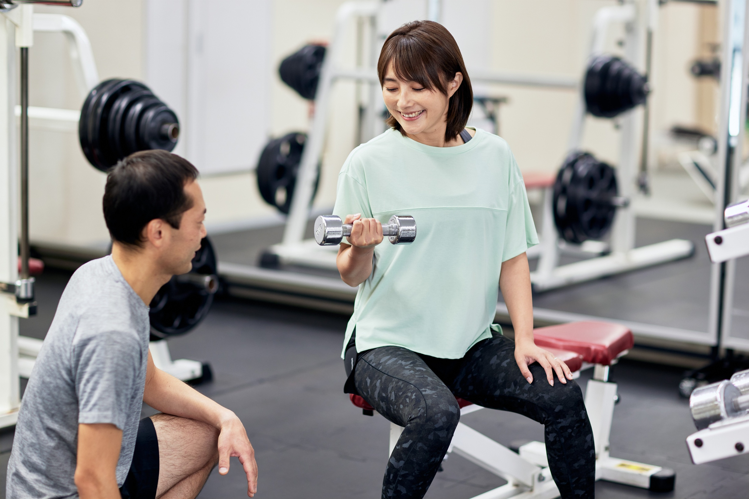 Woman Lifting Dumbbell in Gym with Trainer